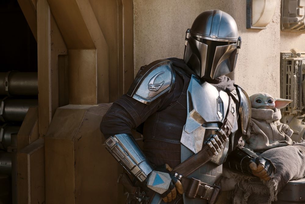 Din Djarin stands outside while shielding Grogu in The Mandalorian Season 2. A sequel movie to the Disney series is slated for 2026.