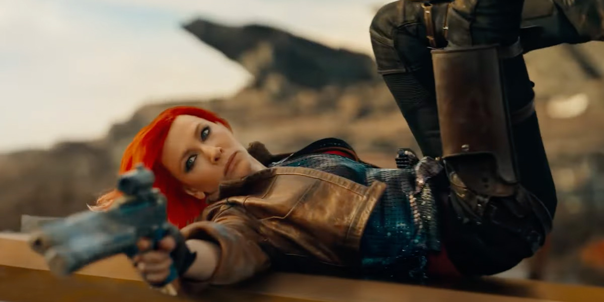 Cate Blanchett as Lilith in Borderlands. She has bright orange hair, is laying to her side, and is pointing a gun.