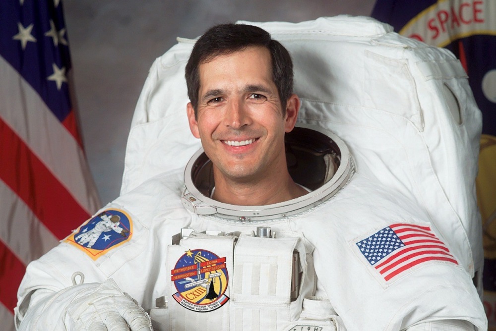El astronauta John B. Herrington se encuentra en su suite espacial frente a la bandera estadounidense.