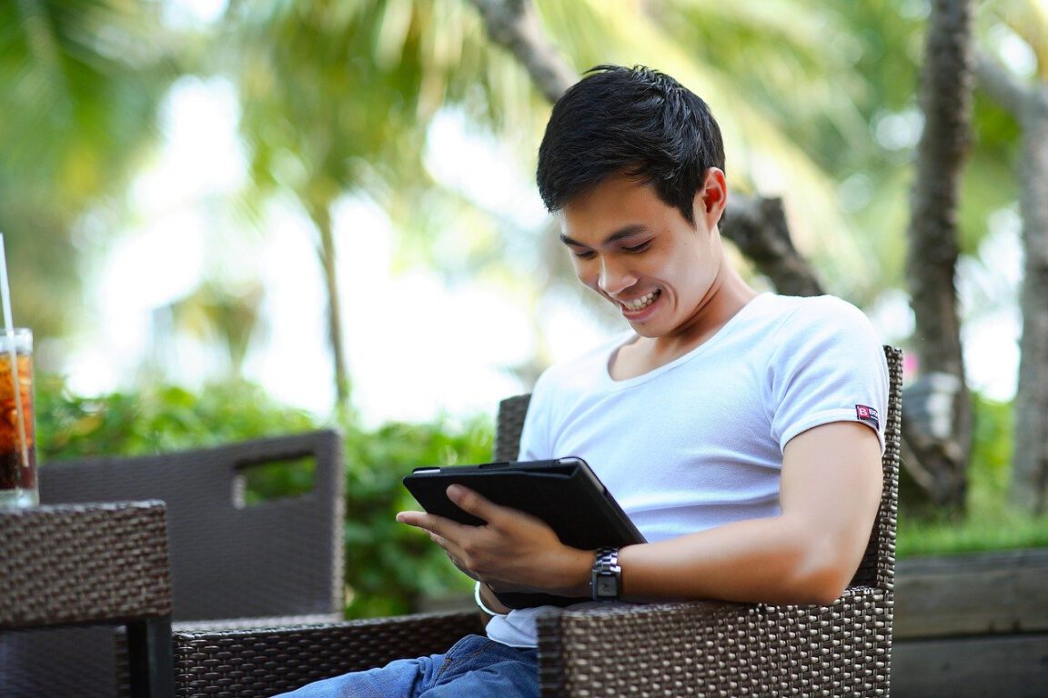 a man sits on a bench smiling and looking at a tablet