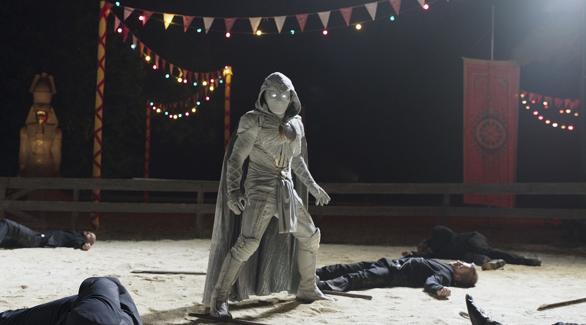 Oscar Isaac as Moon Knight standing among some bodies at night in Marvel's Moon Knight Season 1 Episode 3 The Friendly Type.