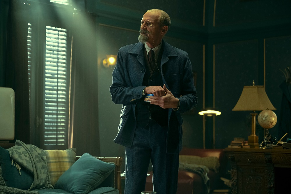 Reginald standing in a living room with his hand in his coat pocket in The Umbrella Academy Season 3 Episode 1 "Meet the Family."