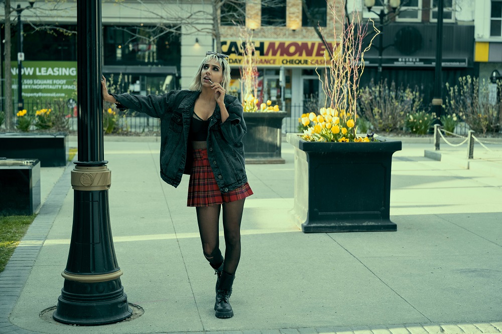 Lila posing on a city sidewalk while resting one hand on a pole on The Umbrella Academy Season 3 Episode 2 "World's Biggest Ball of Twine."