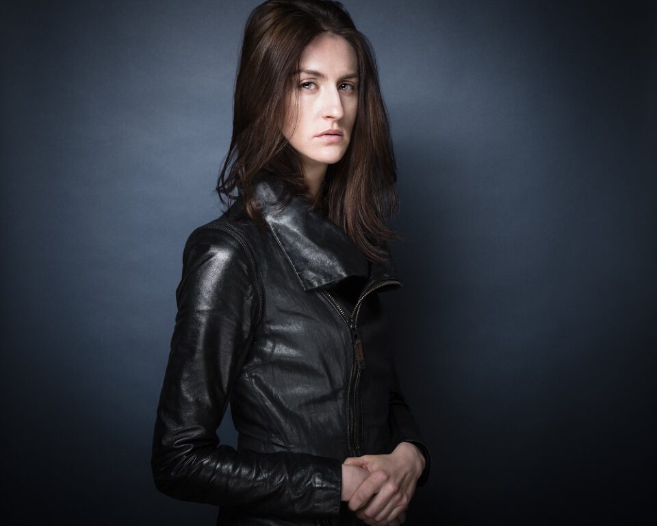 Professional photo of actress and stunt performer Avaah Blackwell wearing a black leather jacket with a dark blue background.