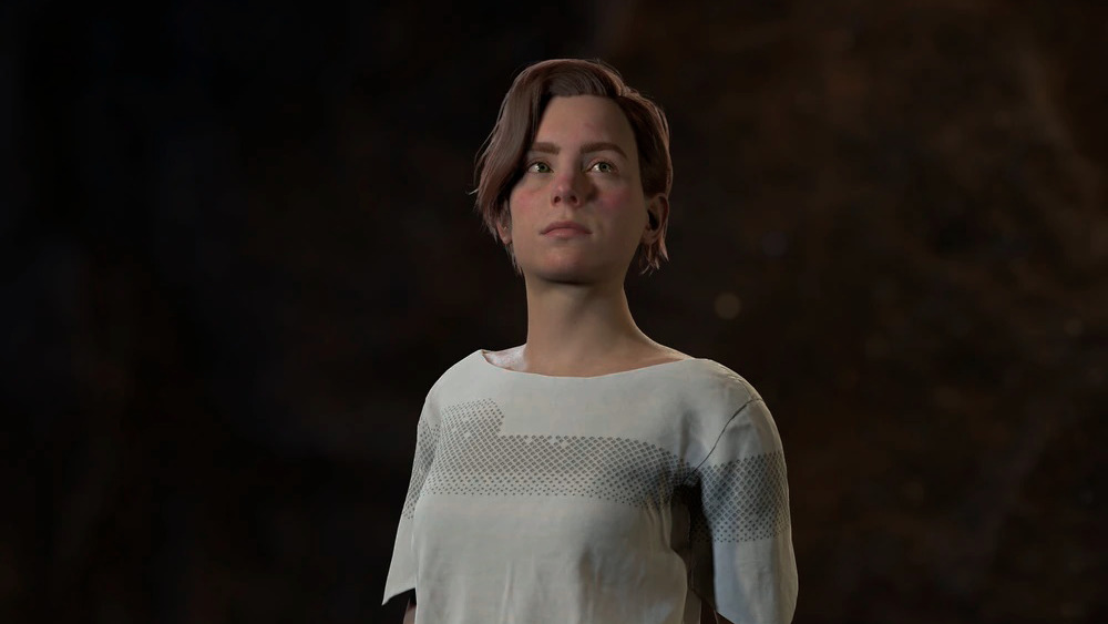Beta, dressed in simple white clothing, looking into the distance. She is a young woman with short, dark hair.