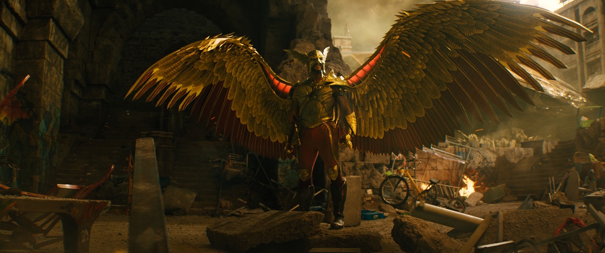 Hawkman spreading his golden wings while standing among debris outside.