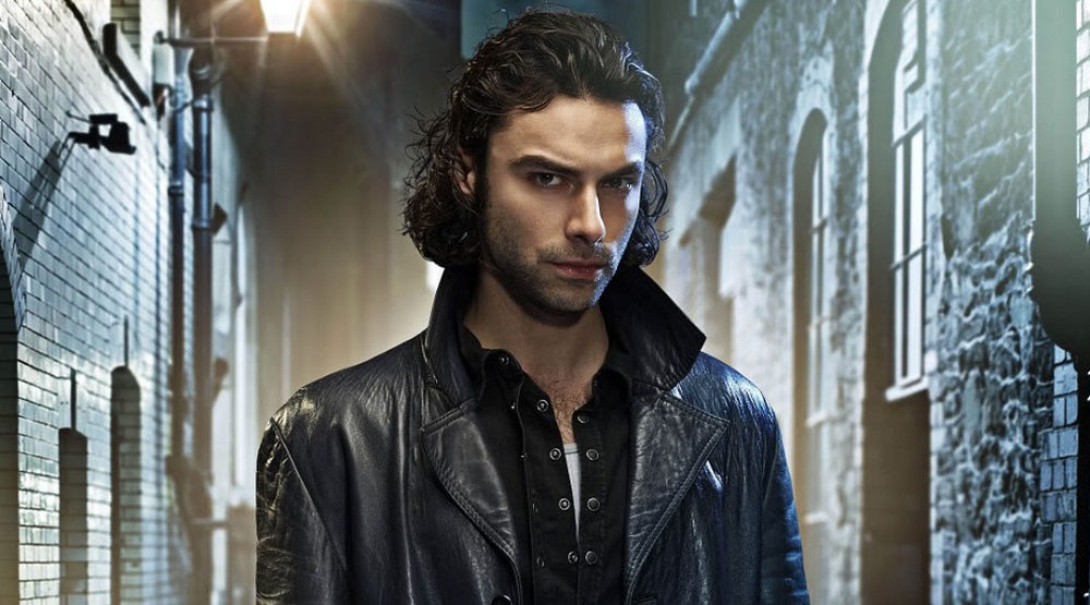 Aidan Turner as John Mitchell, brooding while wearing all black in a dark London alley.