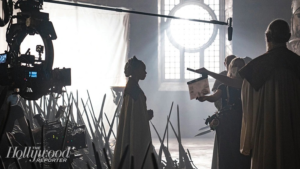 A behind-the-scenes photo from HBO's House of the Dragon, with one woman standing near the Iron Throne with a boom mic over her head.