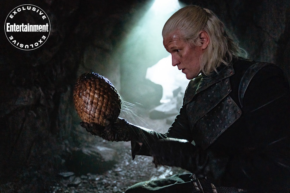 Prince Daemon Targaryen holding a dragon's egg while in a dimly lit cavern.