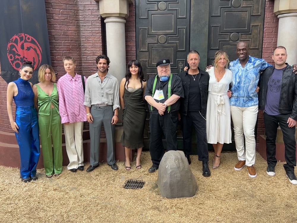 Actors Emily Carey, Milly Alcock, Emma D'Arcy, Fabien Frankel, Olivia Cooke, author George R.R. Martin, Paddy Considine, Eve Best, Steve Toussaint and producer/writer Ryan Condal standing in front of the House of the Dragon "Dragon's Den" exhibit at SDCC 2022.