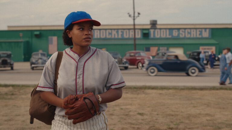 Max Chapman stands in front of the Rockford Tool & Screw Factory while wearing a baseball uniform on A League of Their Own Season 1 Episode 8 "Perfect Game."