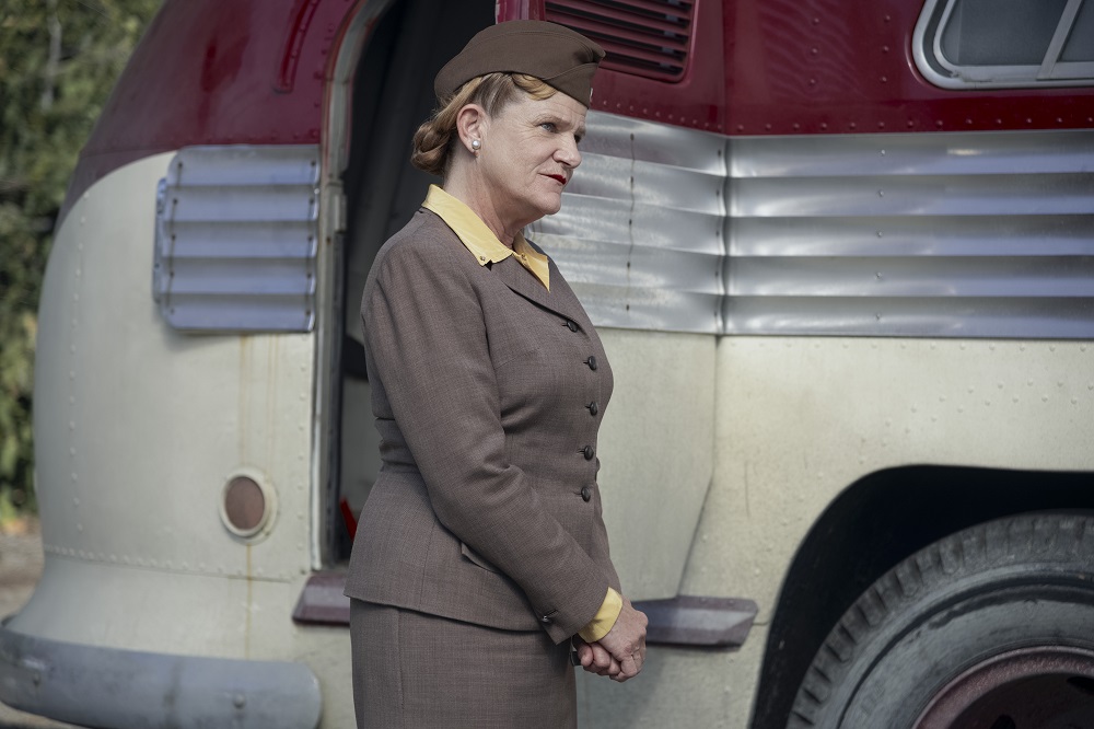 Beverly stands in front of a bus outside while smiling on A League of Their Own Season 1 Episode 8 "Perfect Game."