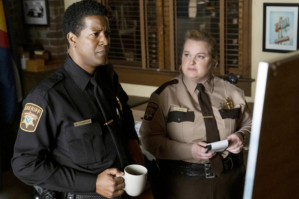 Sheriff Mike Thompson and Deputy Liv Baker stand before an evidence board at the station while mulling over a murder case on Resident Alien Season 2 Episode 9 "Autopsy."