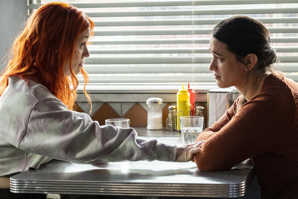 D'Arcy and Asta sit across from each other at a diner while talking on Resident Alien Season 2 Episode 11, "The Weight."