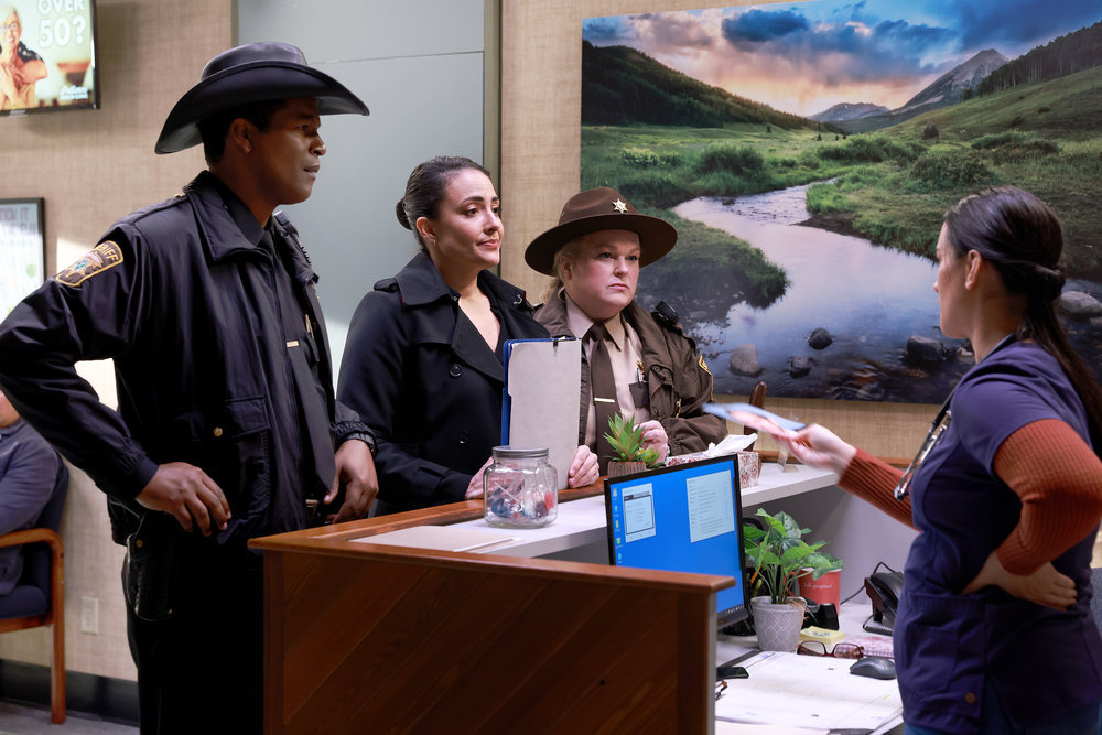 Sheriff Mike, Detective Lena and Deputy Liv question Asta at the Patience Health Clinic on Resident Alien Season 2 Episode 11, "The Weight."