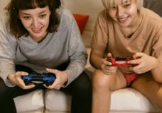 two young women sit on a couch and play video games