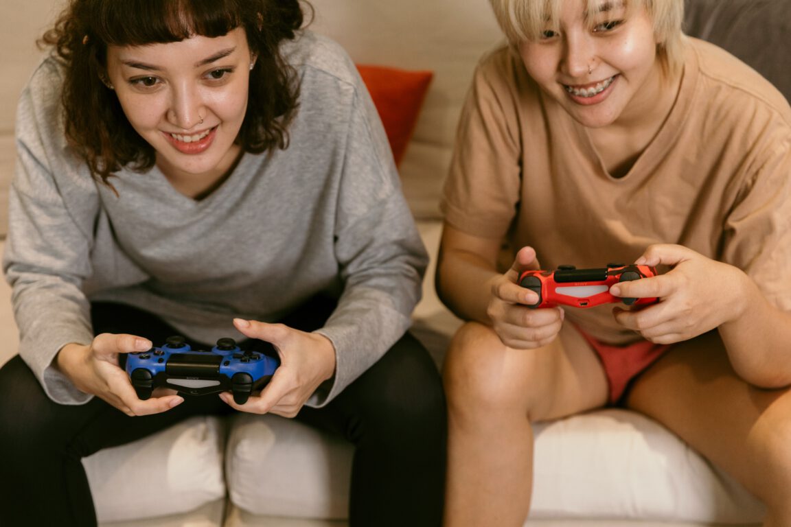 two young women sit on a couch and play video games