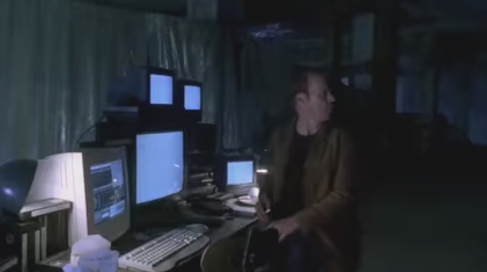 Michael Keaton sitting at a bank of computer monitors