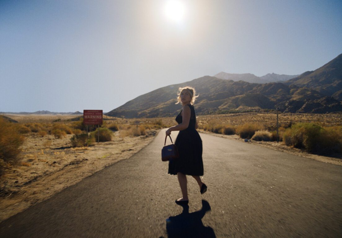 Alice runs down an empty road in a sunny desert in Don't Worry Darling