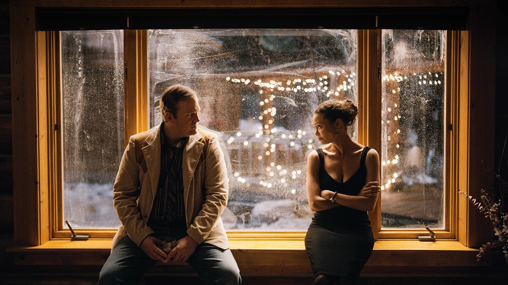 Wolf and Sandra sit on a window sill during a holiday party with a snowy scene behind them in God's Country.