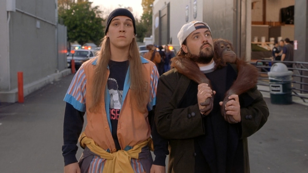 Jay and Silent Bob with a monkey on their backs standing in a Hollywood movie theatre.