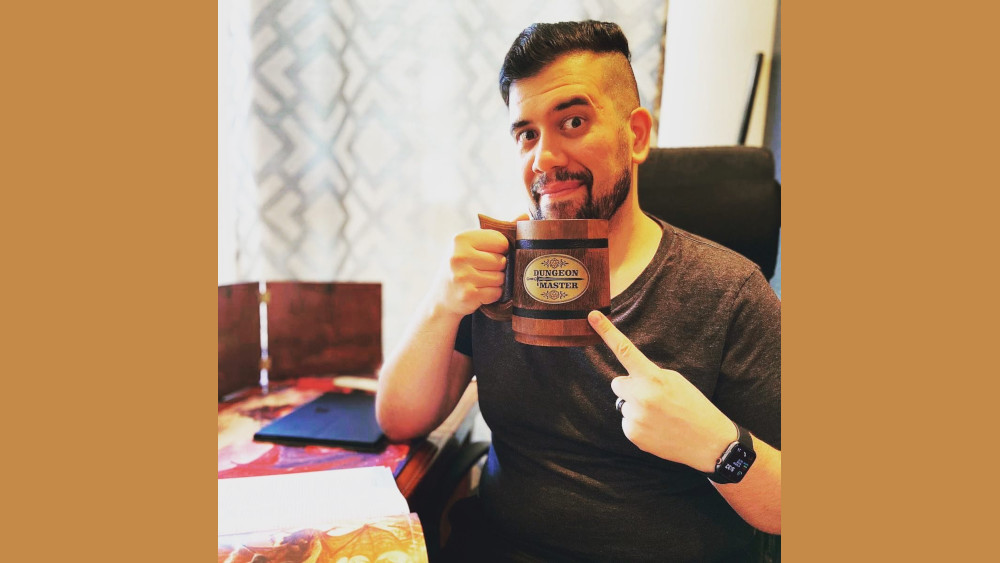 Jake Ynzunza holding a mug that reads "Dungeon Master" while sitting at his desk.