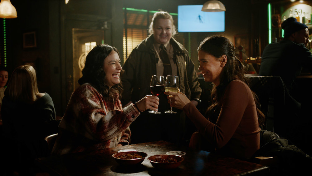Kayla and Kate enjoy some wine in The 59 pub while Deputy Liv walks in during Resident Alien Season 2 Episode 15, "Best of Enemies."