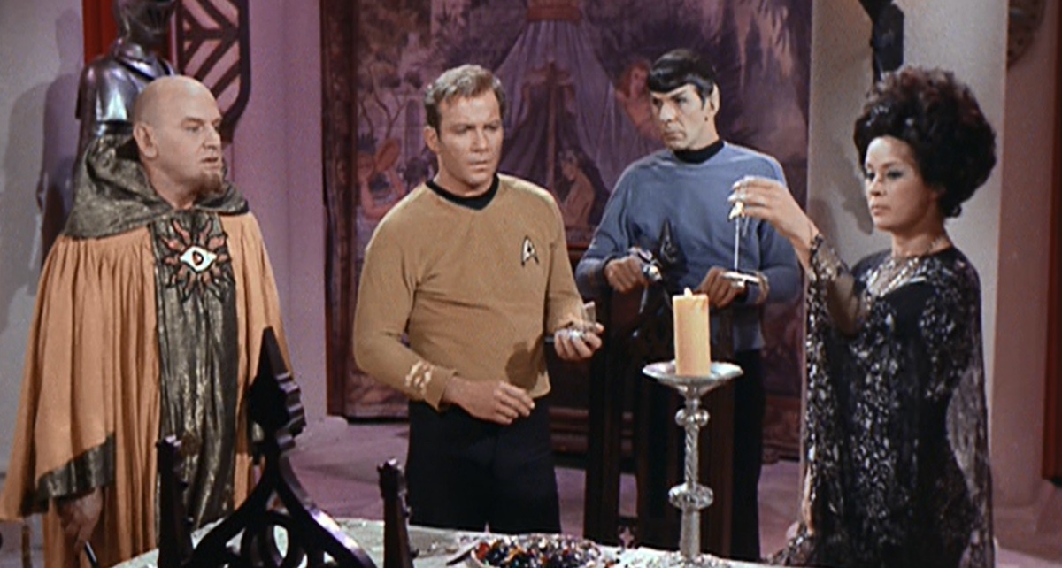 Korob (Theo Marcuse), Kirk (William Shatner), Spock (Leonard Nimoy) and Sylvia (Antoinette Bower). Sylvia dangles a tiny Enterprise on a chain over a candle flame. From TOS season 2 episode 7, "Catspaw."