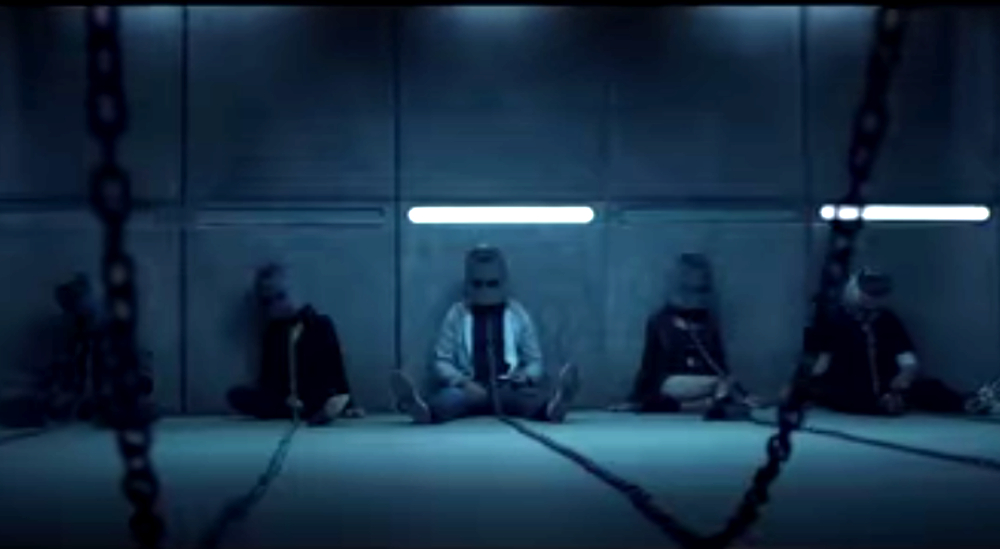 A group of people sit on the floor with helmets on and chained to the wall