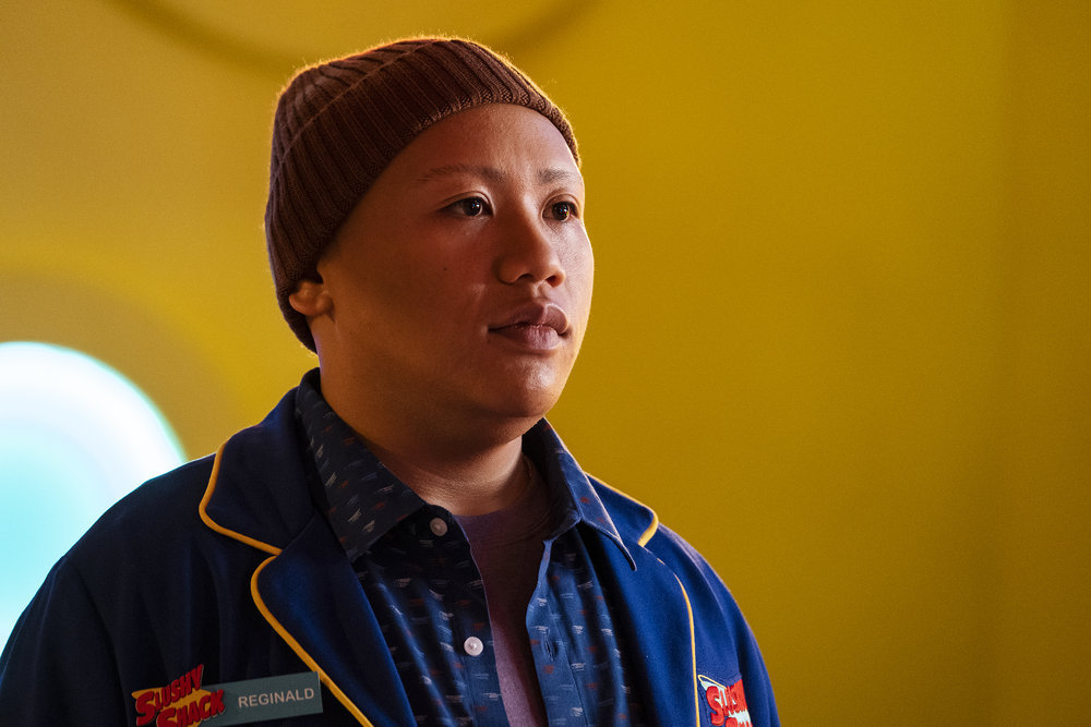 Reginald Andres stares blankly at something off screen while wearing a blue button-down jacket and a brown cap in Reginald the Vampire Season 1 Episode 1, "Dead Weight."