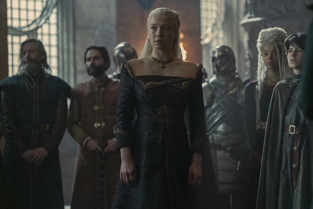 Rhaenyra Targaryen stands in the throne room while wearing a black dress with red trim and looking pensive in House of the Dragon Season 1 Episode 8, "The Lord of the Tides."