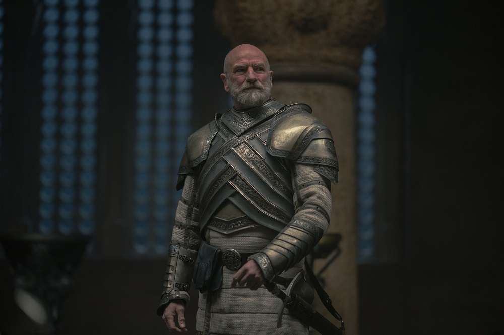 Ser Harrold Westerling stands in his full armor with a hand on his sword while looking suspicious in House of the Dragon Season 1 Episode 9, "The Green Council."