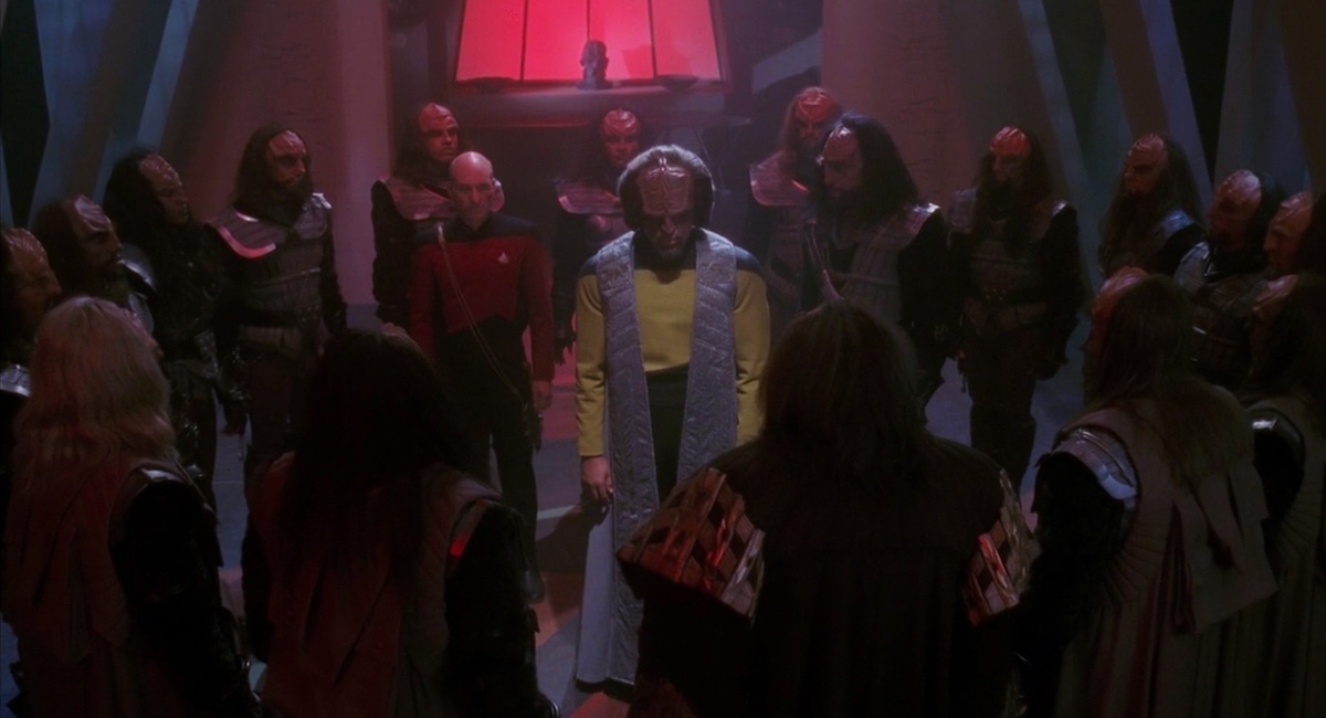 In Star Trek: The Next Generation, Worf (Michael Dorn) stands beside Jean-Luc Picard (Patrick Stewart). They both wear their Starfleet uniforms. They are surrounded by a ring of Klingons in traditional garb. From TNG.