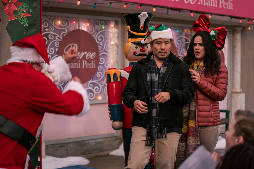 Timmy and Eliza stand close together outside in the snow while wearing festive Christmas attire in Blockbuster Season 1.
