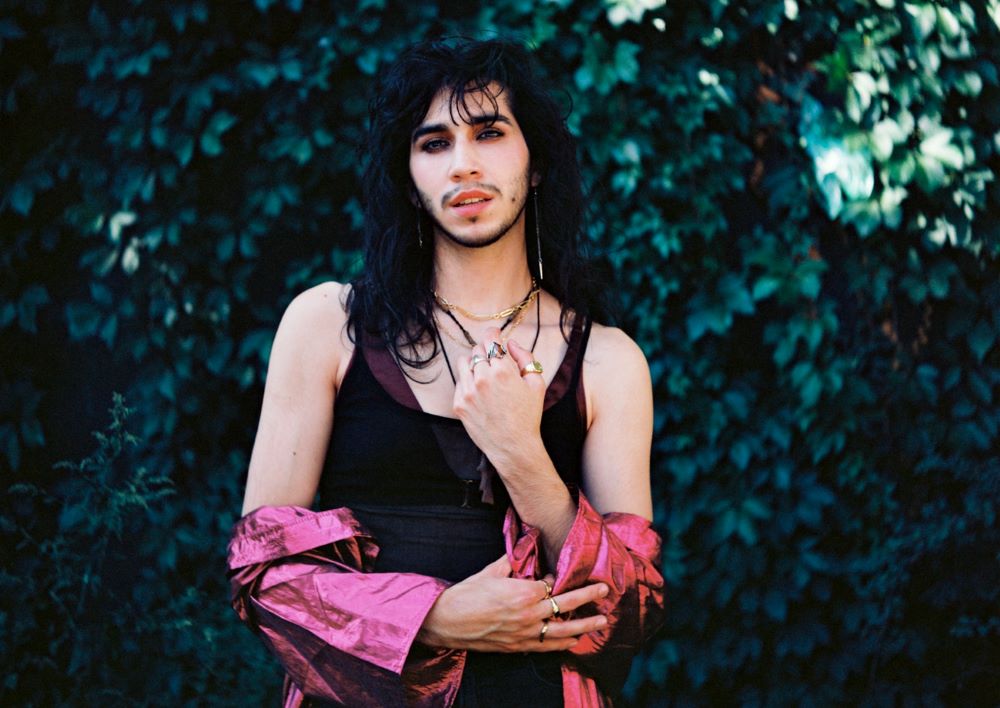 Actor Heath V. Salazar poses outside while wearing a black tank top and pink sash.