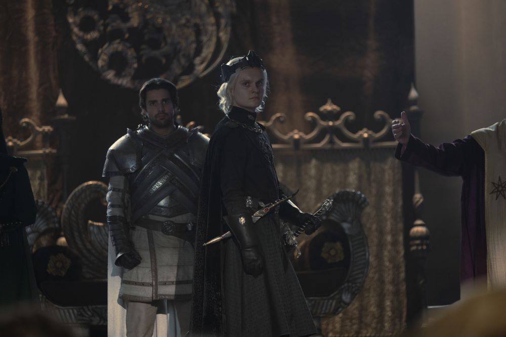 King Aegon II Targaryen wears an all-black outfit while turning to face a crowd of people during his coronation in House of the Dragon Season 1 Episode 9, "The Green Council."