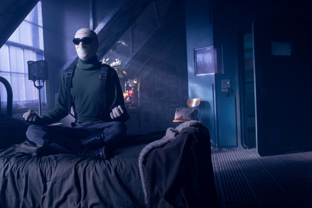 Larry sits cross-legged on his bed in his dimly lit bedroom in Doom Patrol Season 4 Episode 5, "Youth Patrol."