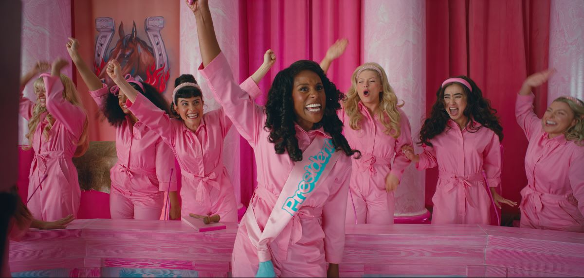 Issa Rae wears a bright pink outfit with a sash that says "President" while waving and smiling in the Barbie movie.