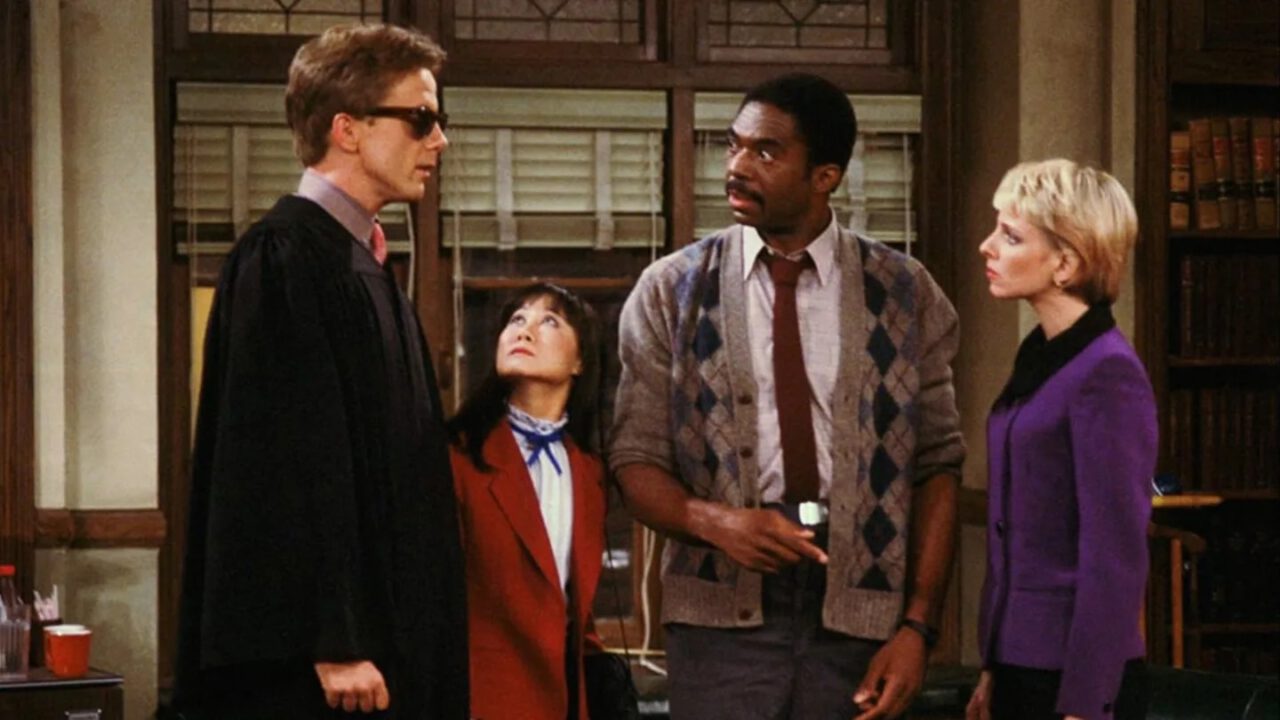 Harry Anderson, Charles Robinson, Ellen Foley and Denice Kumagai talk in an office in Night Court.