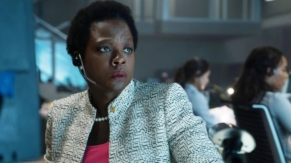 Amanda Waller, played by Viola Davis, wearing a white blazer and a headset and looking serious.