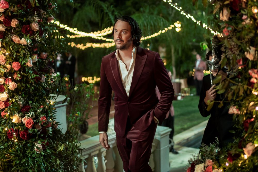 Lasher wears a burgundy velvet suit while walking through a lavish outdoor party in Mayfair Witches Season 1 Episode 1, "The Witching Hour."