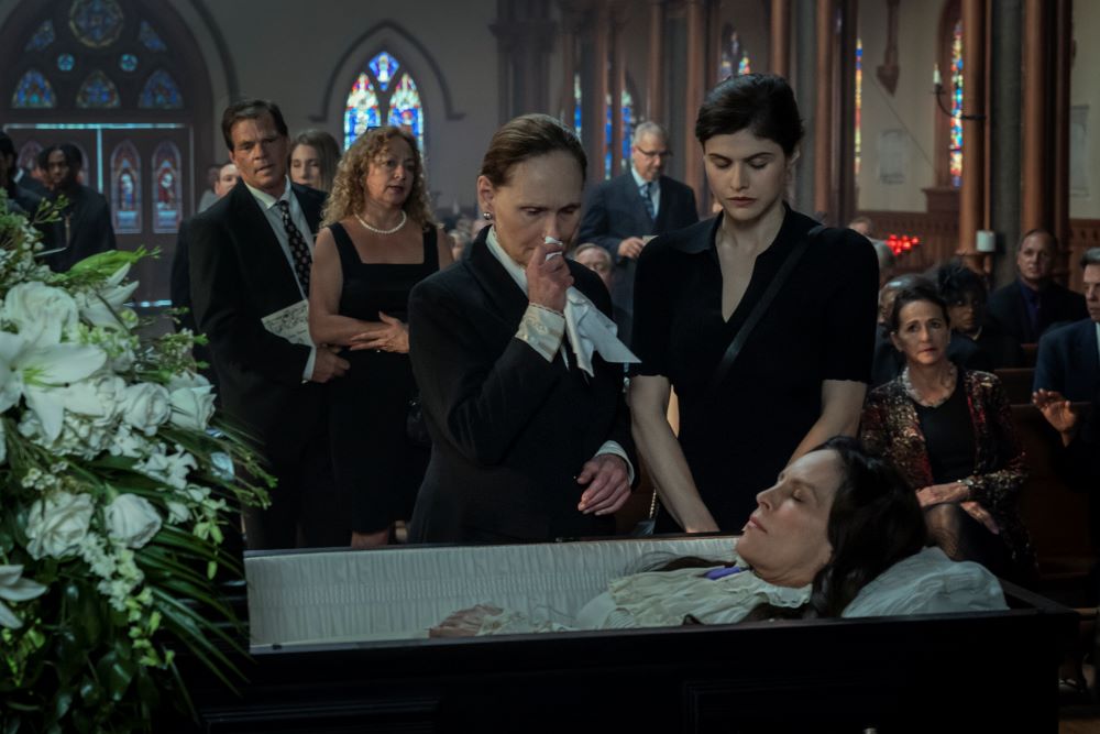 Carlotta Mayfair and Rowan Fielding stand over Deirdre Mayfair's open coffin while looking somber in Mayfair Witches Season 1 Episode 4, "Curiouser and Curiouser."