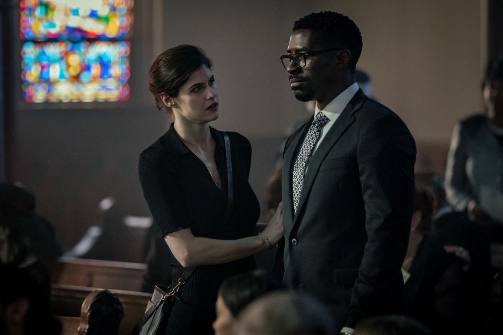 Rowan Fielding and Ciprien Grieve stand in the sanctuary of a church for a funeral while Rowan places her hand on Ciprien's arm in Mayfair Witches Season 1 Episode 4, "Curiouser and Curiouser."
