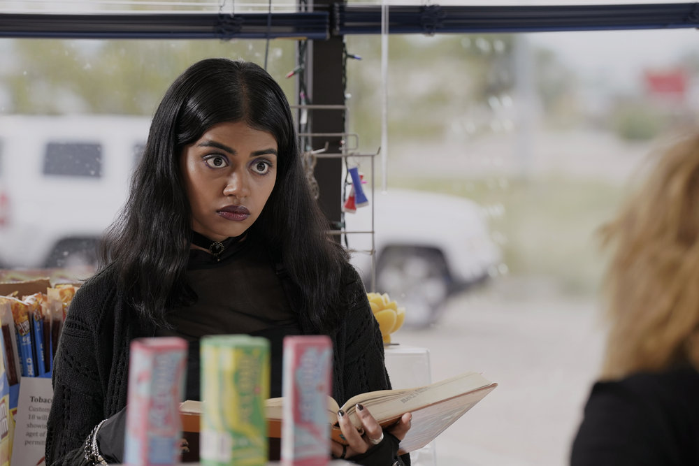 Sara stands behind the cash register in the mini mart while looking focused in Poker Face Season 1 Episode 2, "The Night Shift."