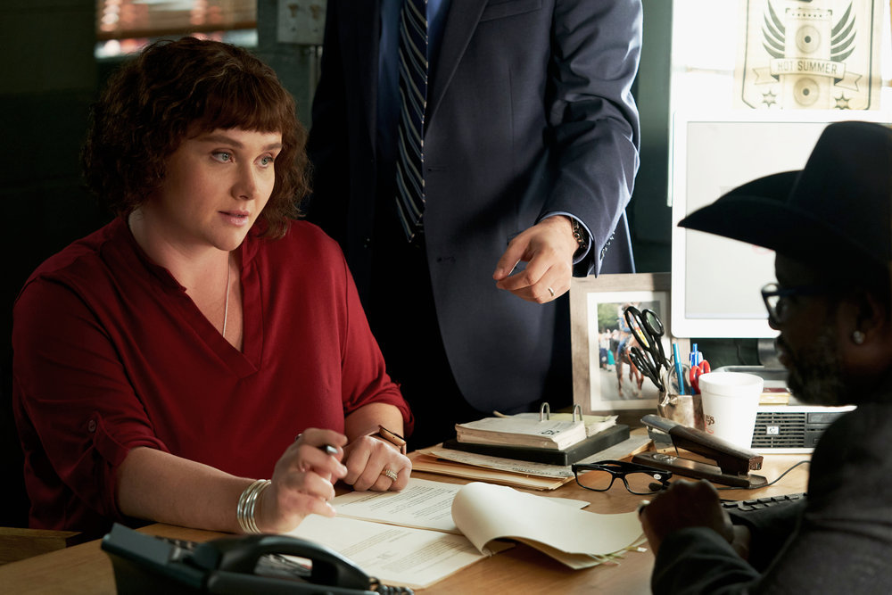 Mandy sits at a desk with a pen in hand and papers in front of her in Poker Face Season 1 Episode 3, "The Stall."