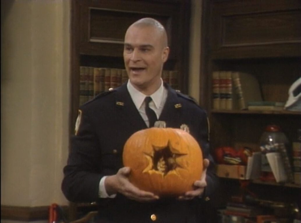 Richard Moll smiles with a pumpkin in his hands in Night Court.
