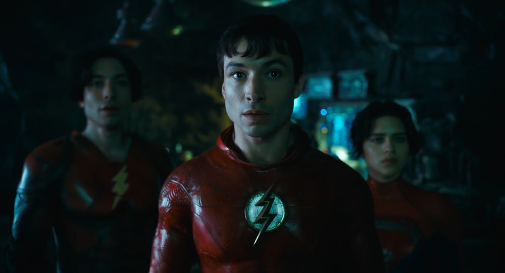 Barry Allen stands next to an alternate timeline version of himself and Kara Zor-El while all three look surprised in the DC film The Flash.