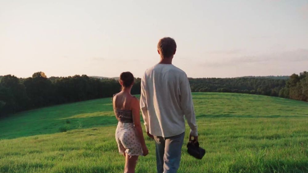 Eliza and Finn walk through an empty green field on a spring day in the film American Cherry.