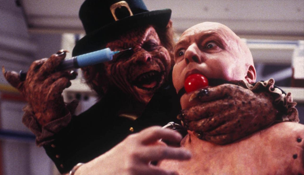 Leprechaun prepares to inject a man with a blue substance.