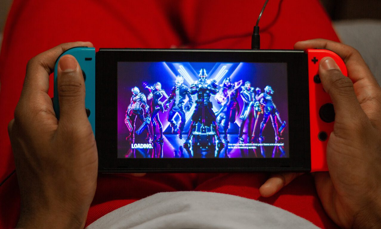 Two hands holding a Nintendo Switch while playing Fortnite. 
